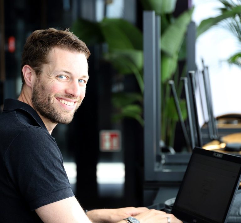 Julian Haug am Laptop Julian Haug sitzt lächelnd an einem Restauranttisch und arbeitet an einem Laptop.