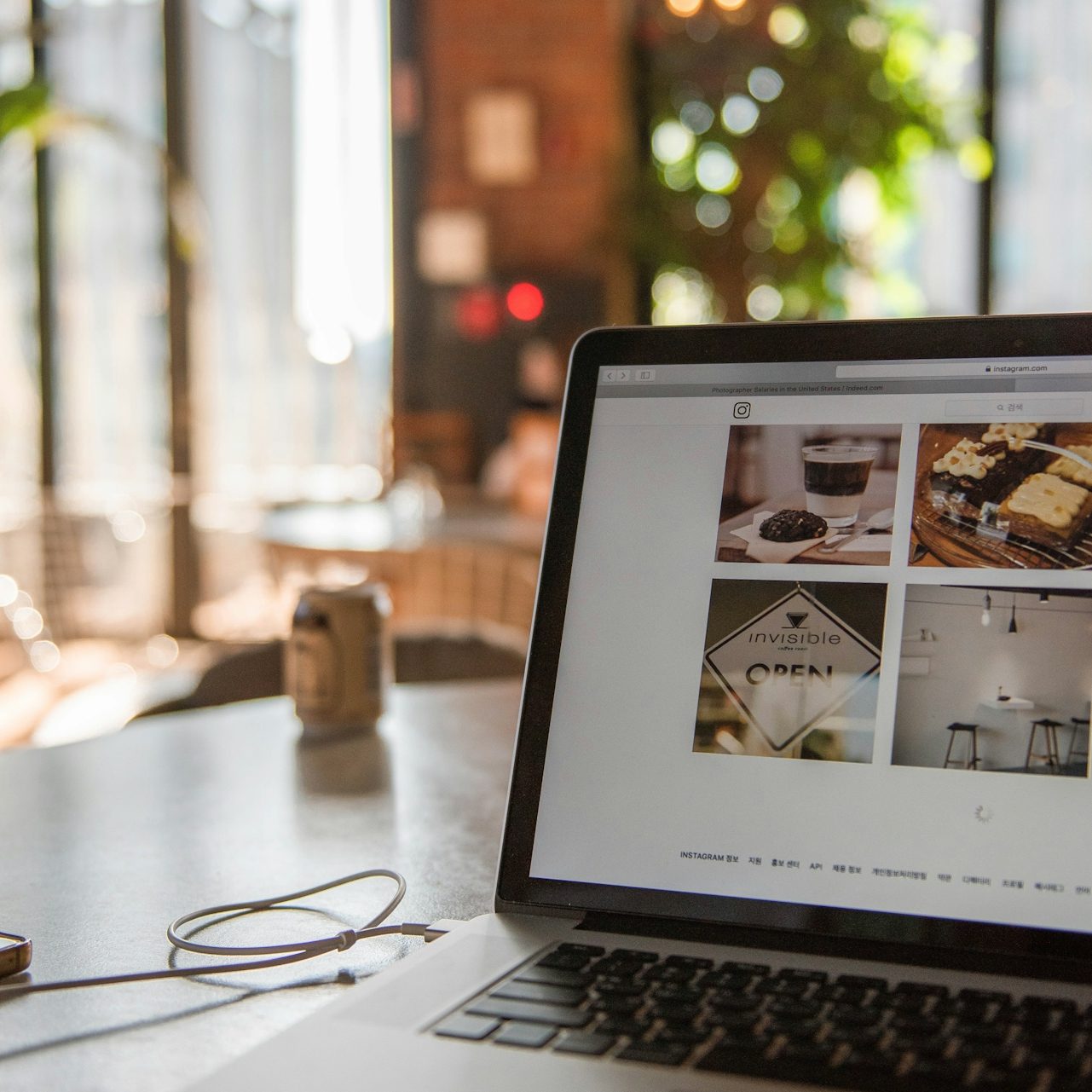 Laptop mit offenem Bildschirm, am Tisch in einem hellen Café, Pflanze im Hintergrund.